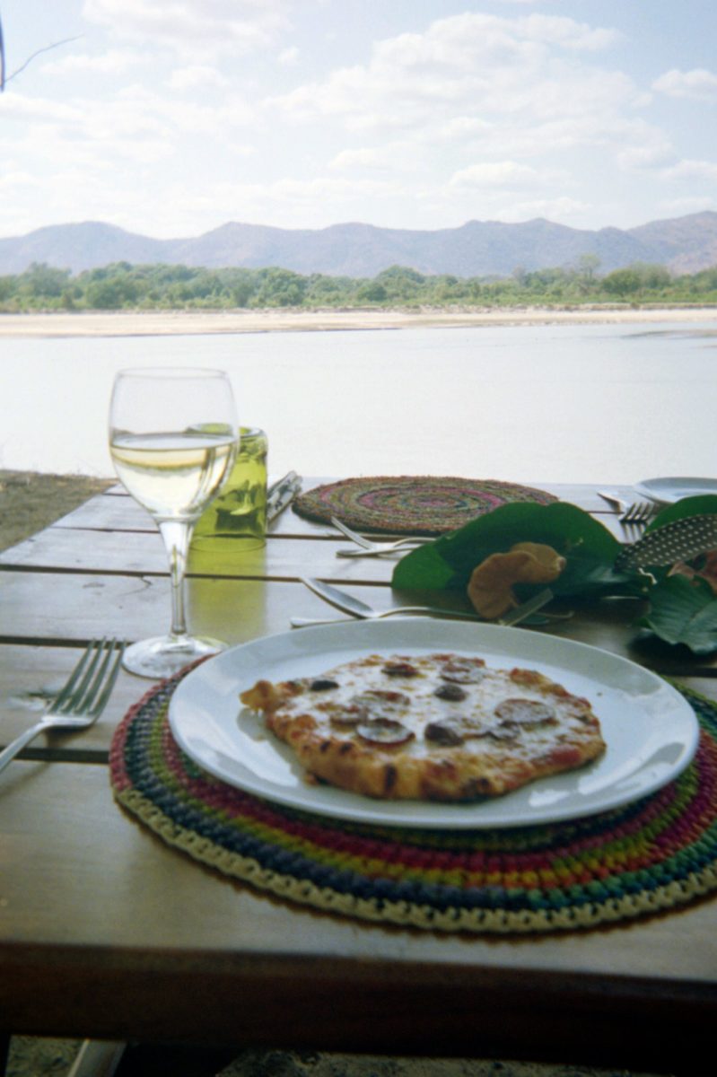 A personal pizza with glass of white wine overlooking a river in zambia's south luangwa national park