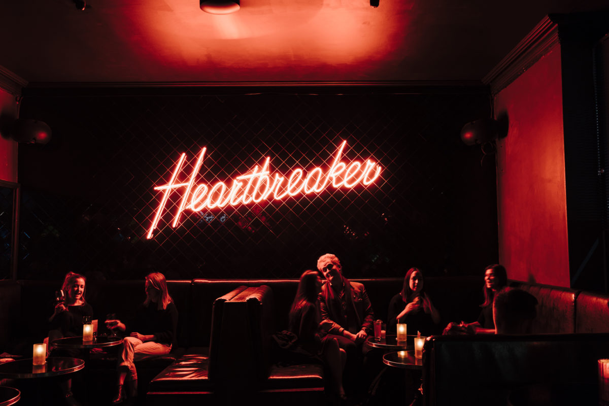 A neon sign reading "Heartbreaker" inside a dark bar.