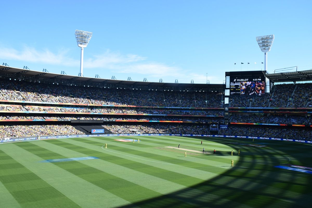 Beneath a blue sky, an enormous sports stadium filled with people.