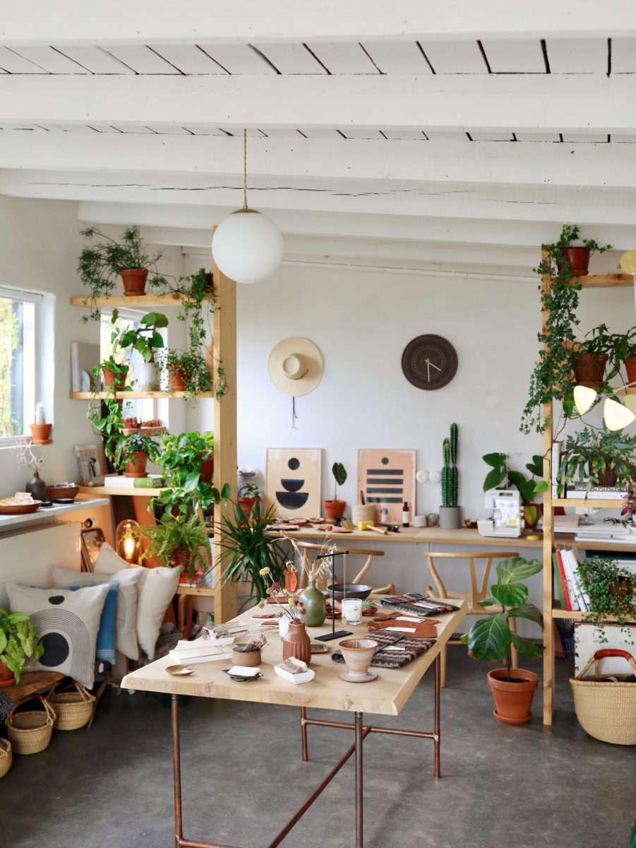 A store with bright white walls containing colorful plants, hats, art, and trinkets.