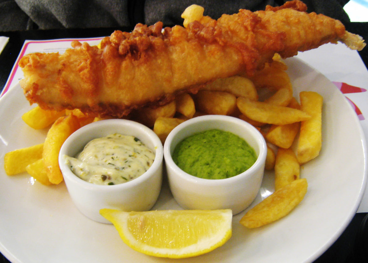 Fish, chips, mushy peas, tartar sauce, and lemon on a white plate