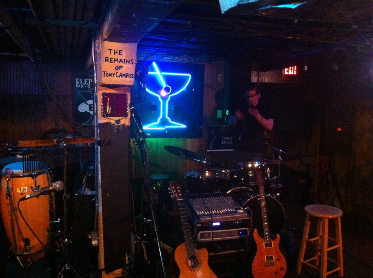 two red guitars sit beneath a neon sign resembling a martini glass inside a dark music venue