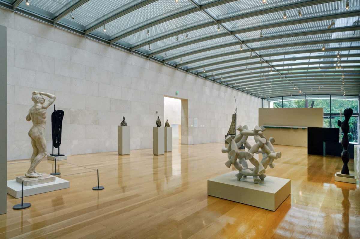 a large white room with light wood floors and a glass ceilling containing several modern sculptures