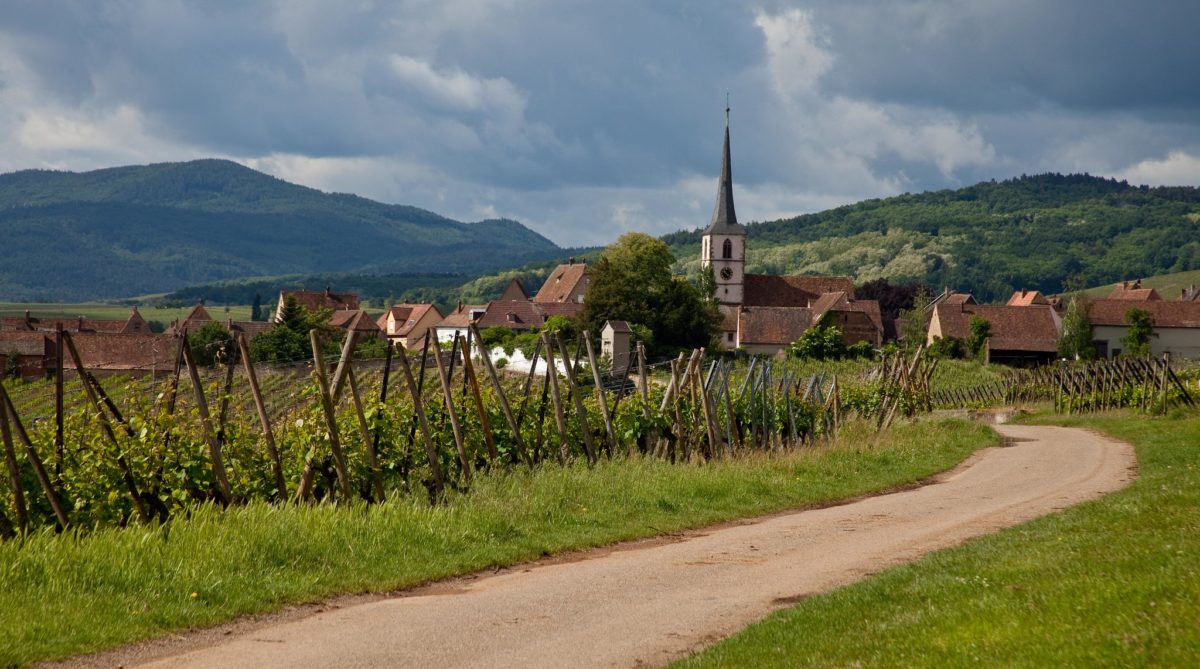 a path leads to a village in the middle of green mountains in the center of which sits a church with a thin gray spire