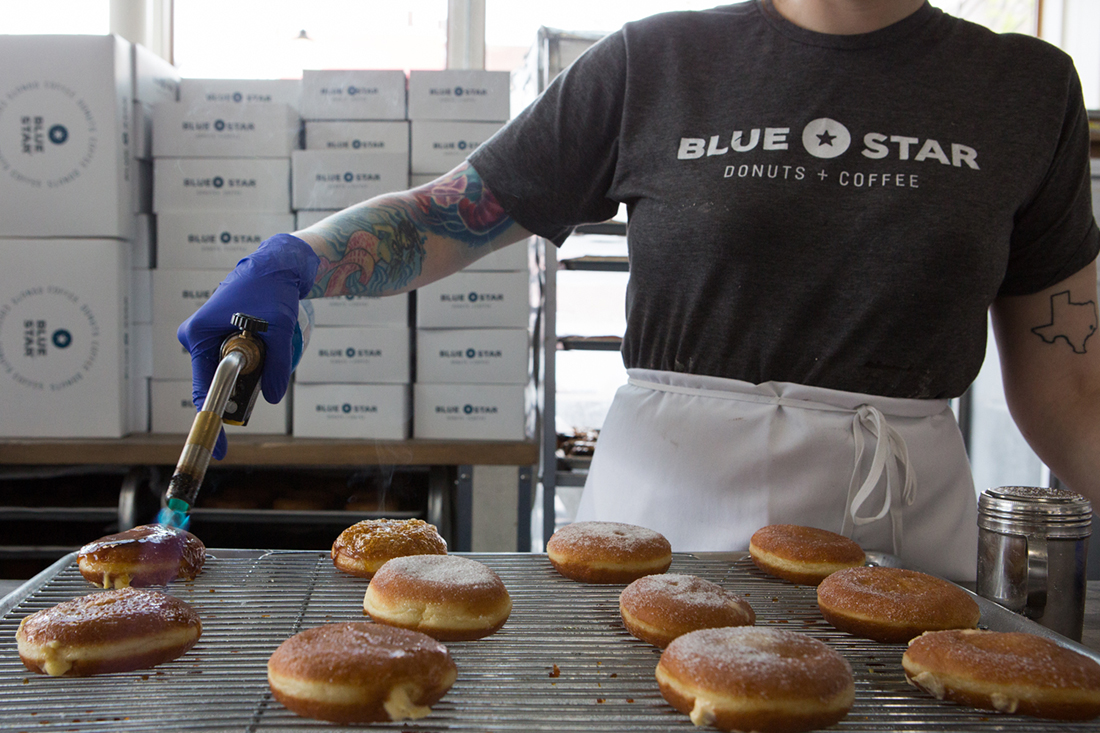 a person wearing gloves and an apron handling donuts laid out on a tray