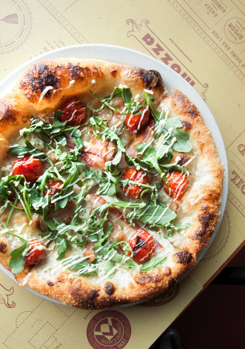 a pizza topped with cherry tomatoes, greens, and shredded cheese