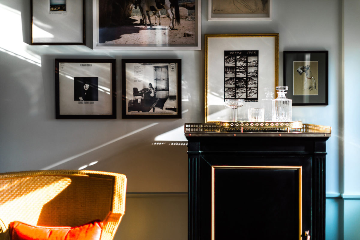 an orange chair and small, dark wood table with glasses on top of it sitting in front of a wall of photographs