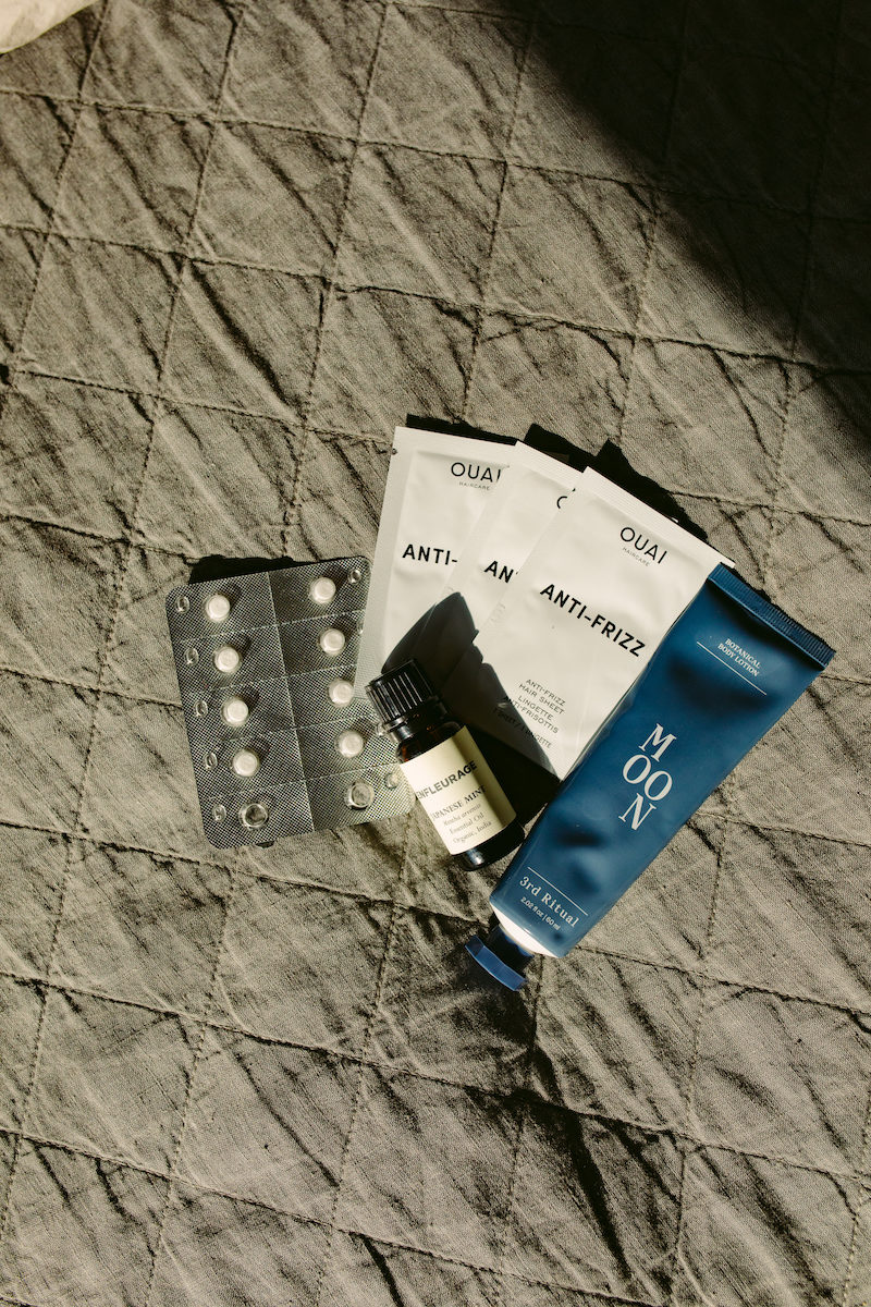 a pack of Claratin pills, anti-frizz wipe packets, and a tube of body lotion on a grey quilt