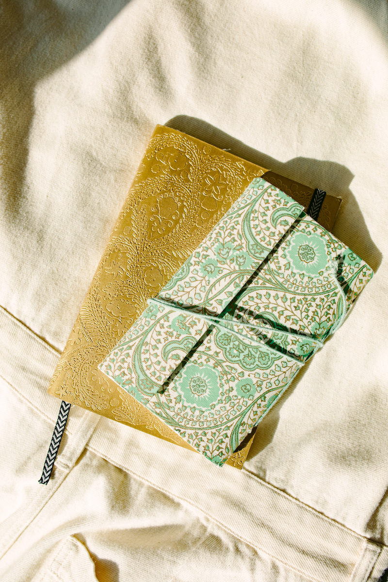 turquoise and gold silk-bound journals on a bed