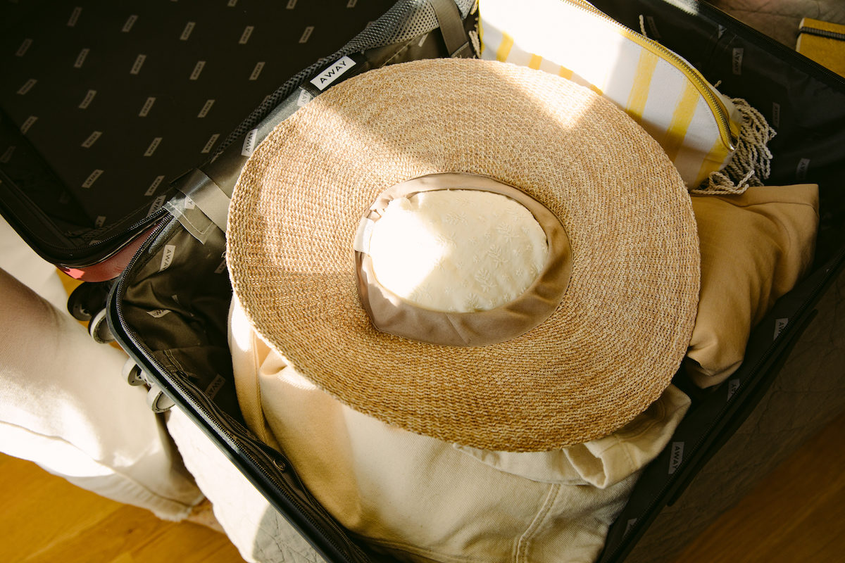 a brimmed straw hat packed in a suitcase with fabric stuffing the head