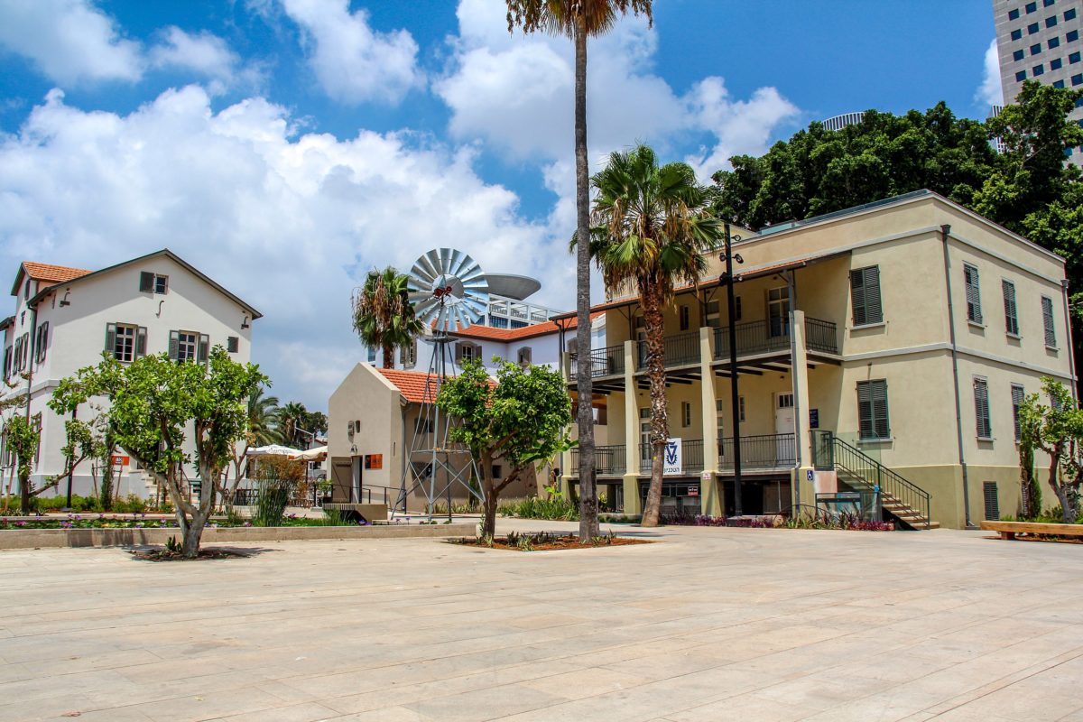 an outdoor plaza with various types of trees and a bright yellow building