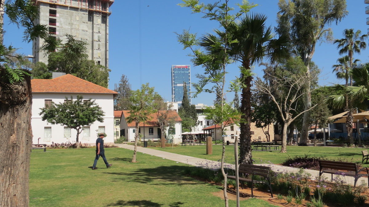 a man walking through small park with several villas and a skyscraper in the distance