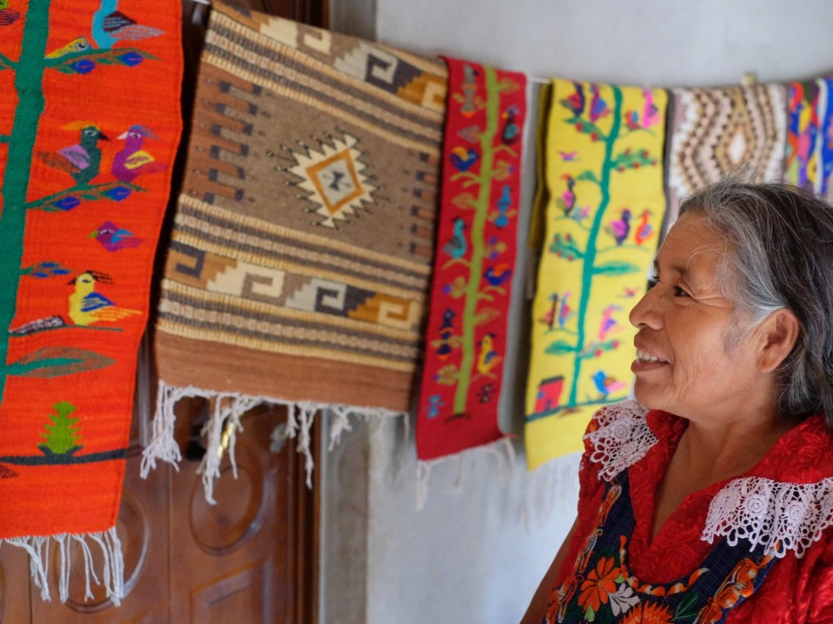 an older woman looking up at colorful tapestries