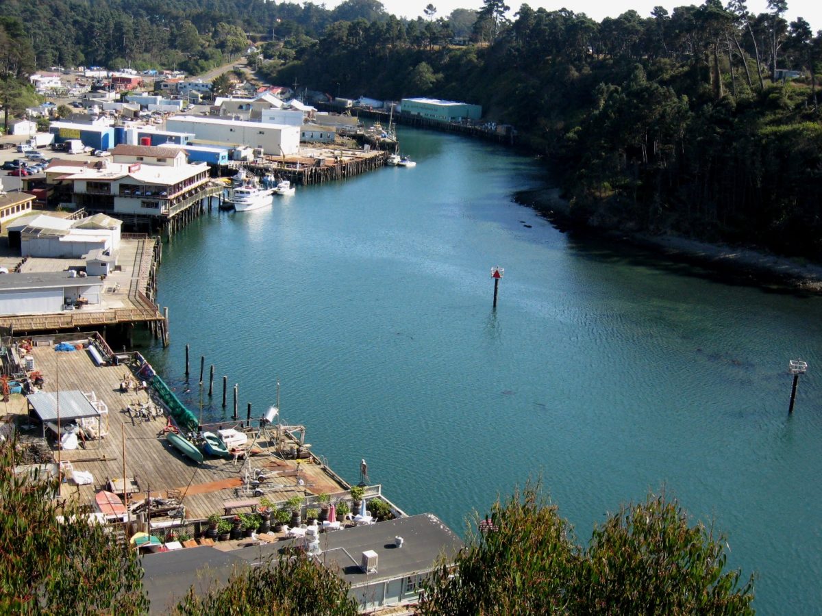 a small port with colorful buildings sits next to a blue harbor