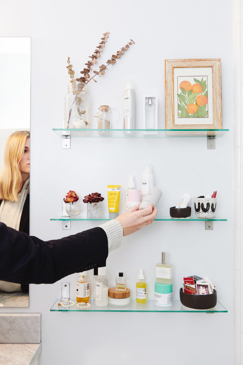 woman reaching towards three bathroom shelves filled with toiletries