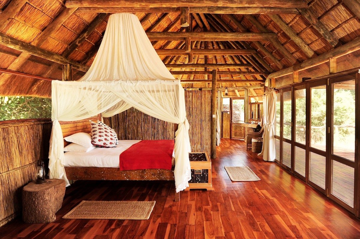 interior of a thatched-roof chalet with mosquito-netted bed