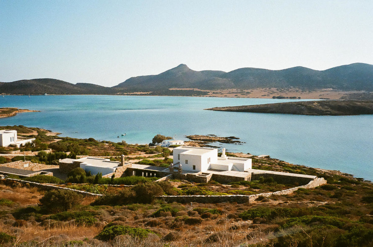 a white house on the sea with mountains in the distance