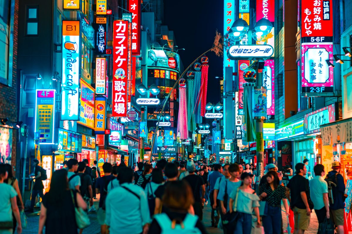 crowds of people walking through Shibuya, a large neighborhood filled with neon signs