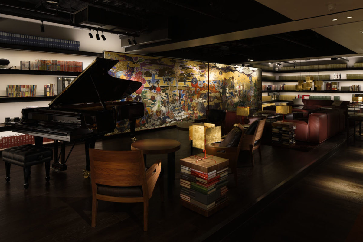 a piano sitting at the front of a dimly-lit room filled with tables, chairs, and books