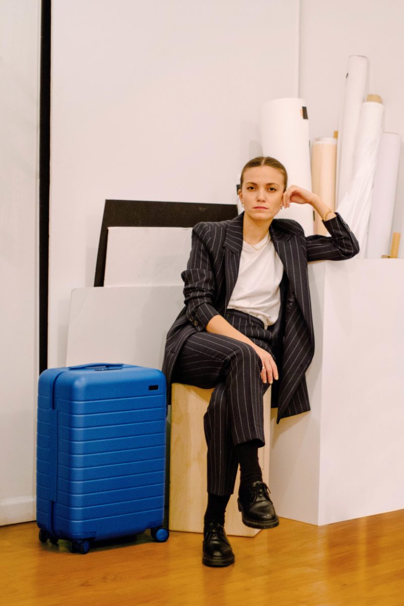 a woman in a suit sits on top of a suitcase