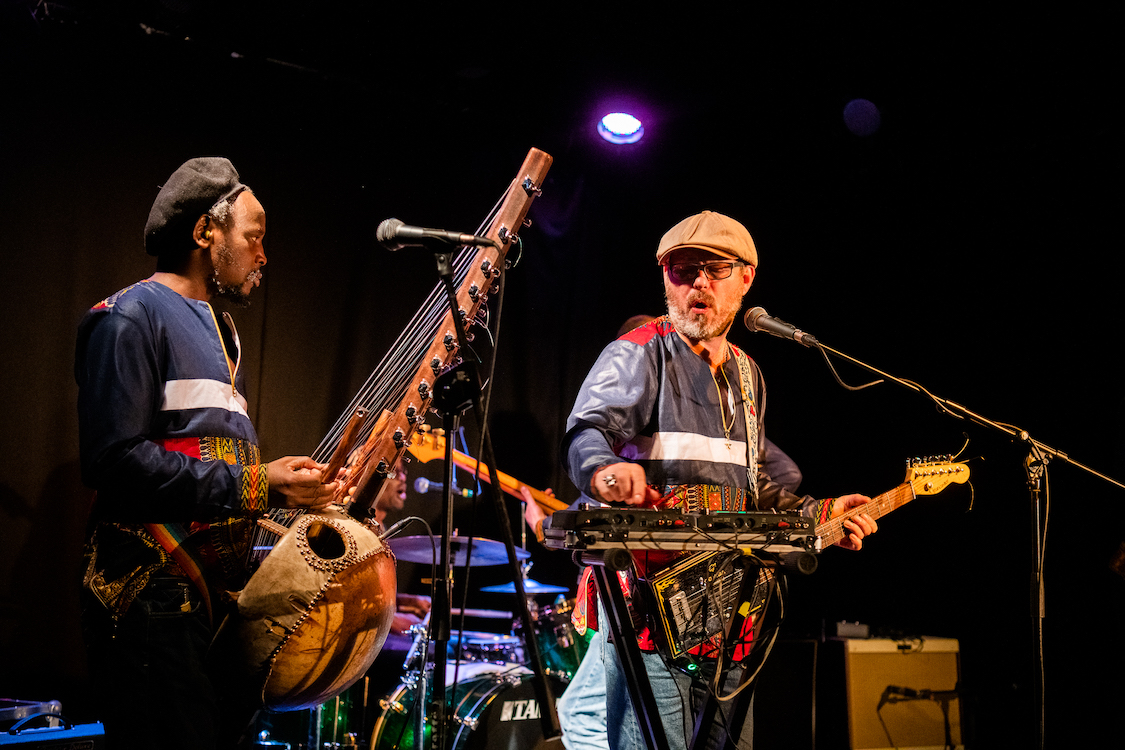 two members of a band playing a series of instruments on stage