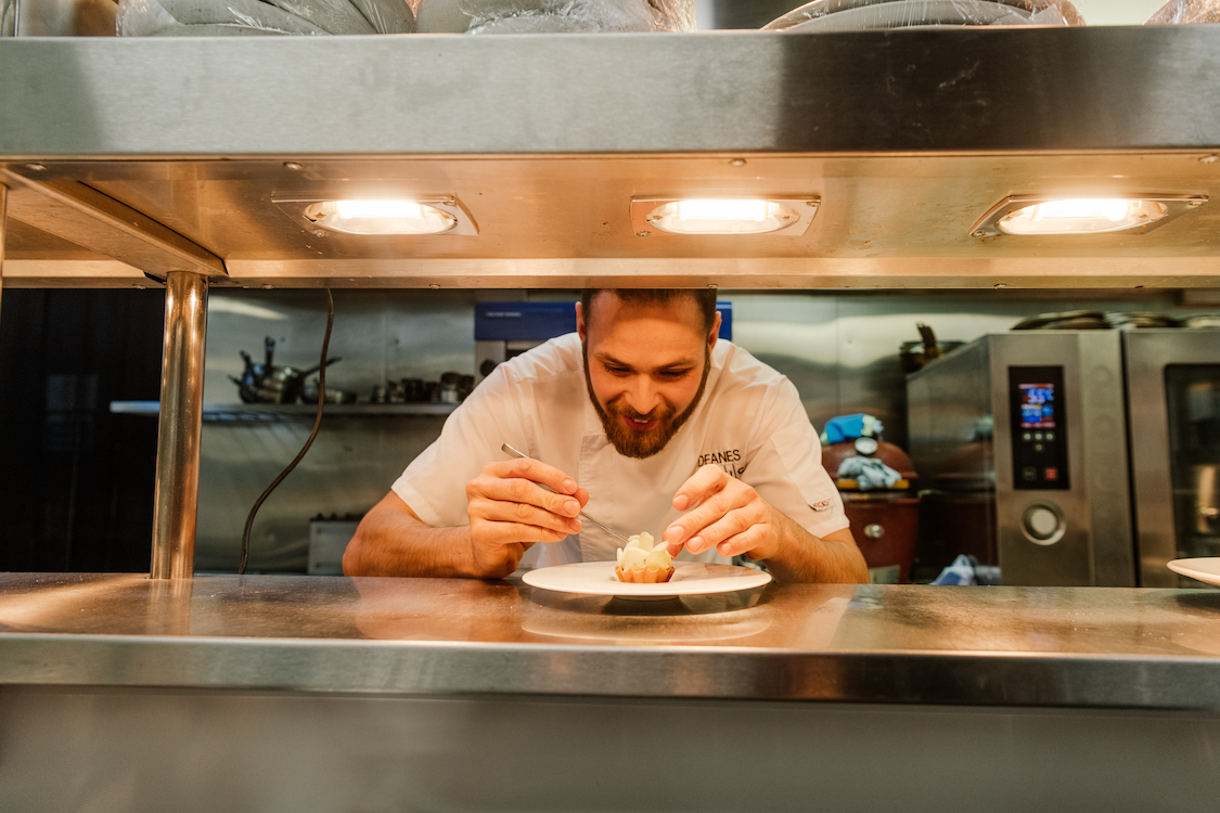 a chef works on a small pastry beneath a kitchen light