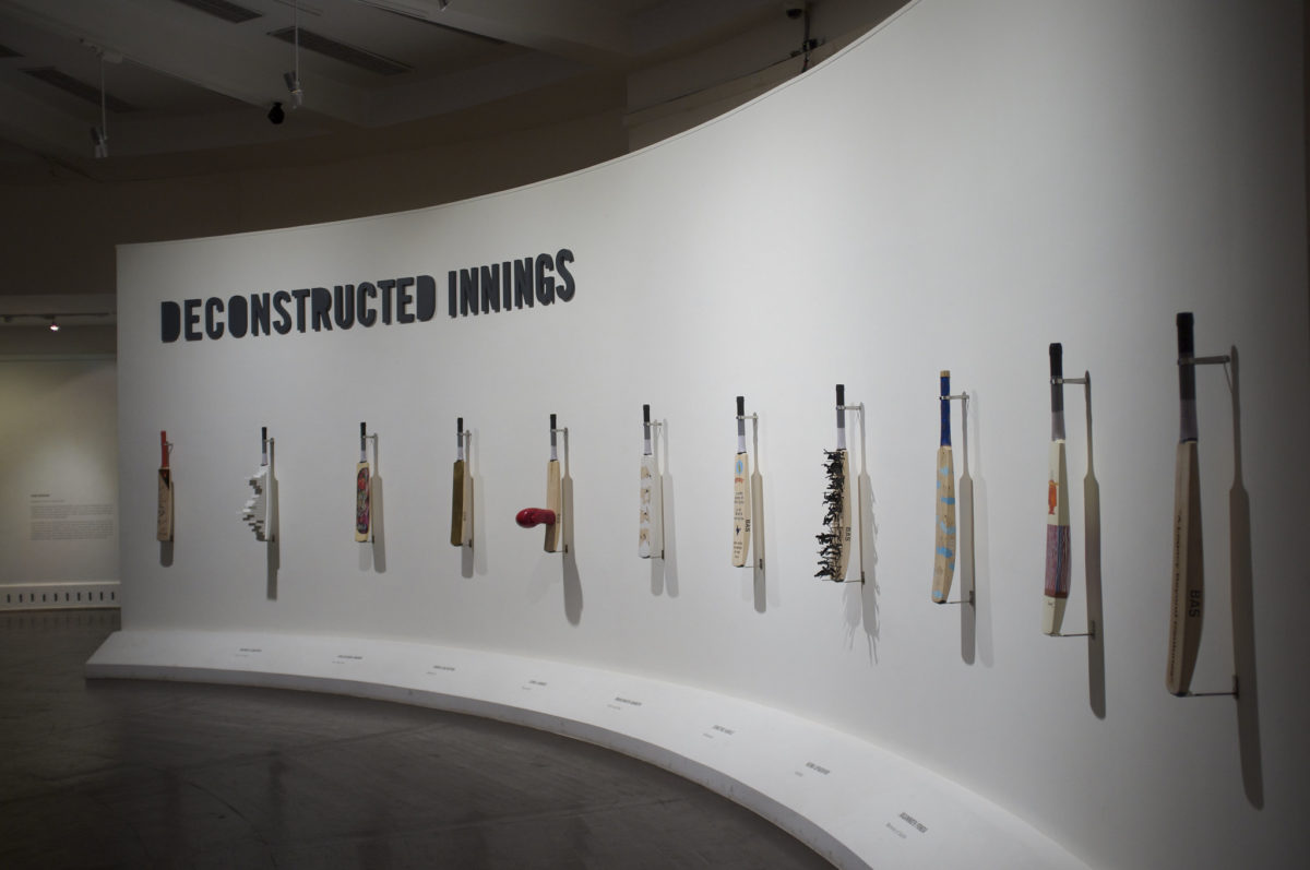 deconstructed and embellished cricket bats hanging on an exhibition wall inside a museum