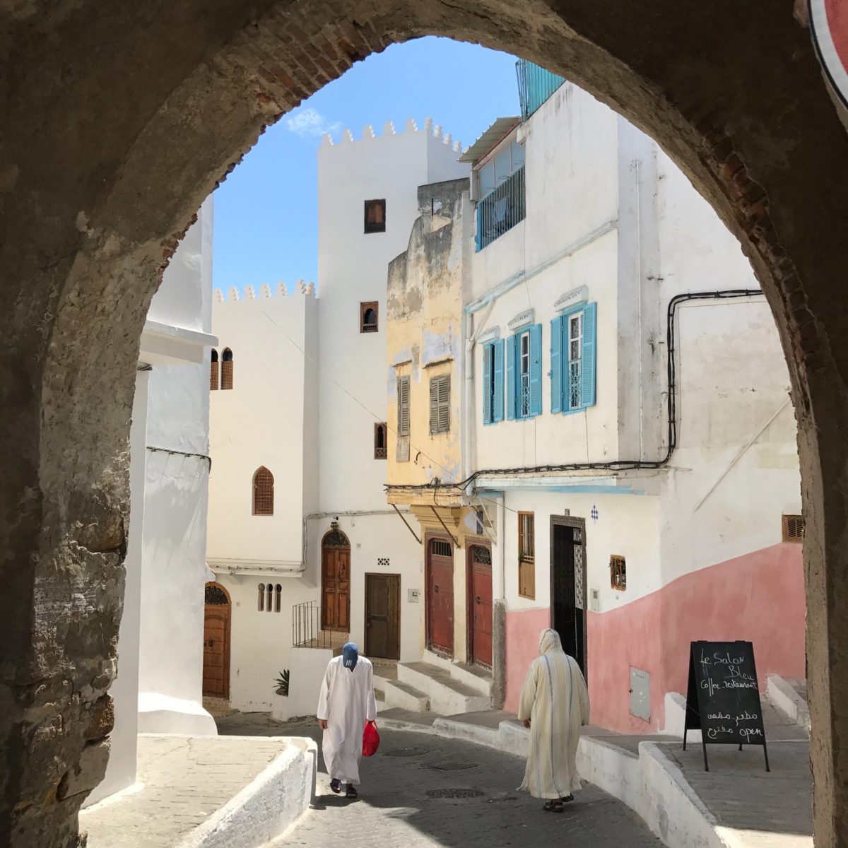 two people in robes walking down a cobblestone alleyway on a sunny day