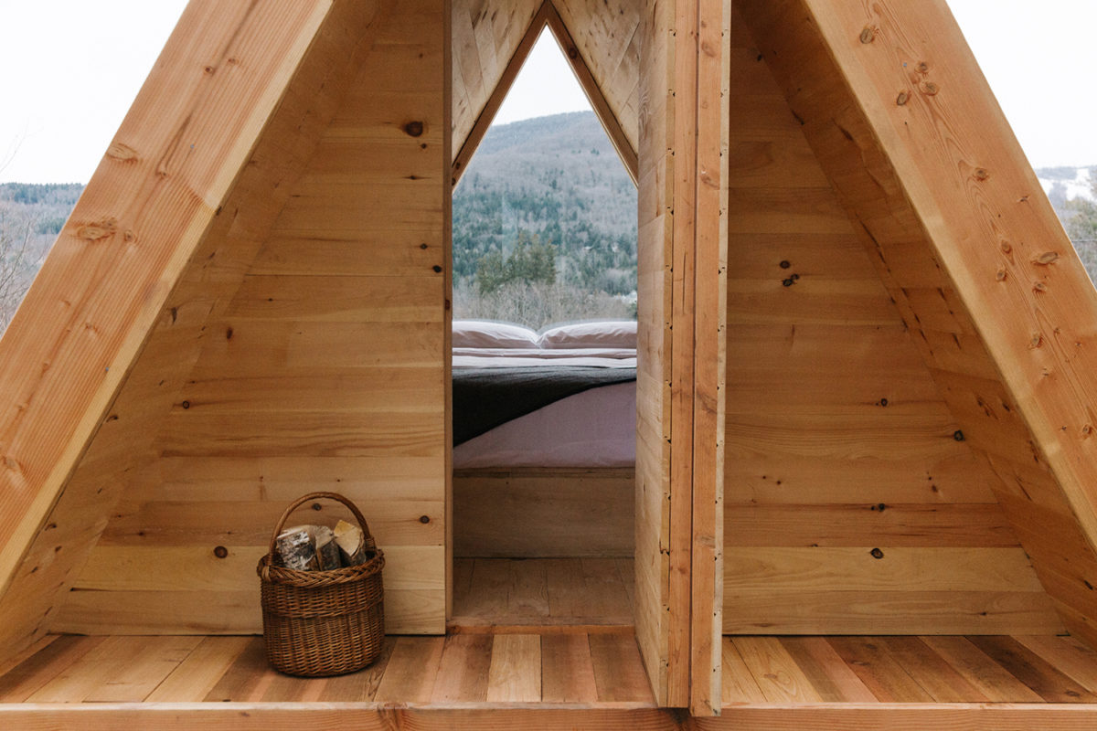 a wooden tent with a bed overlooking hills