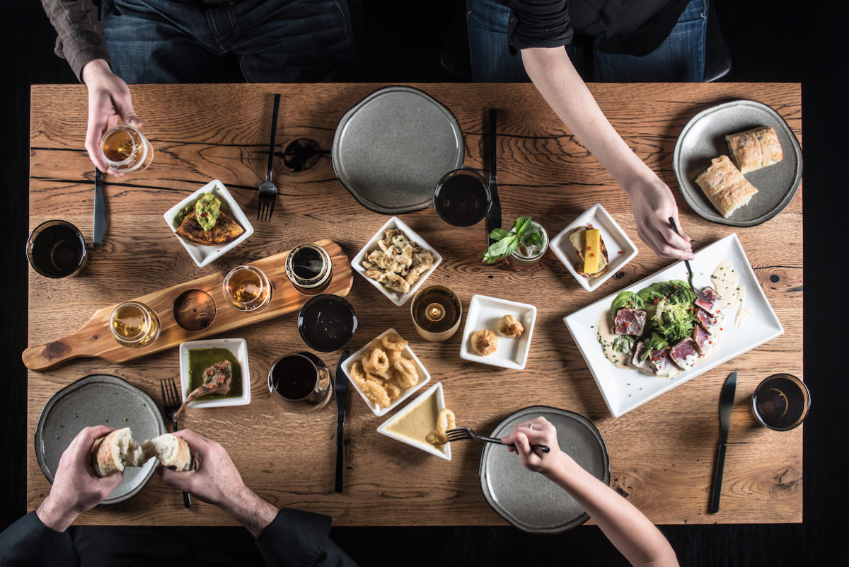 people reaching out towards plates on a table full of food