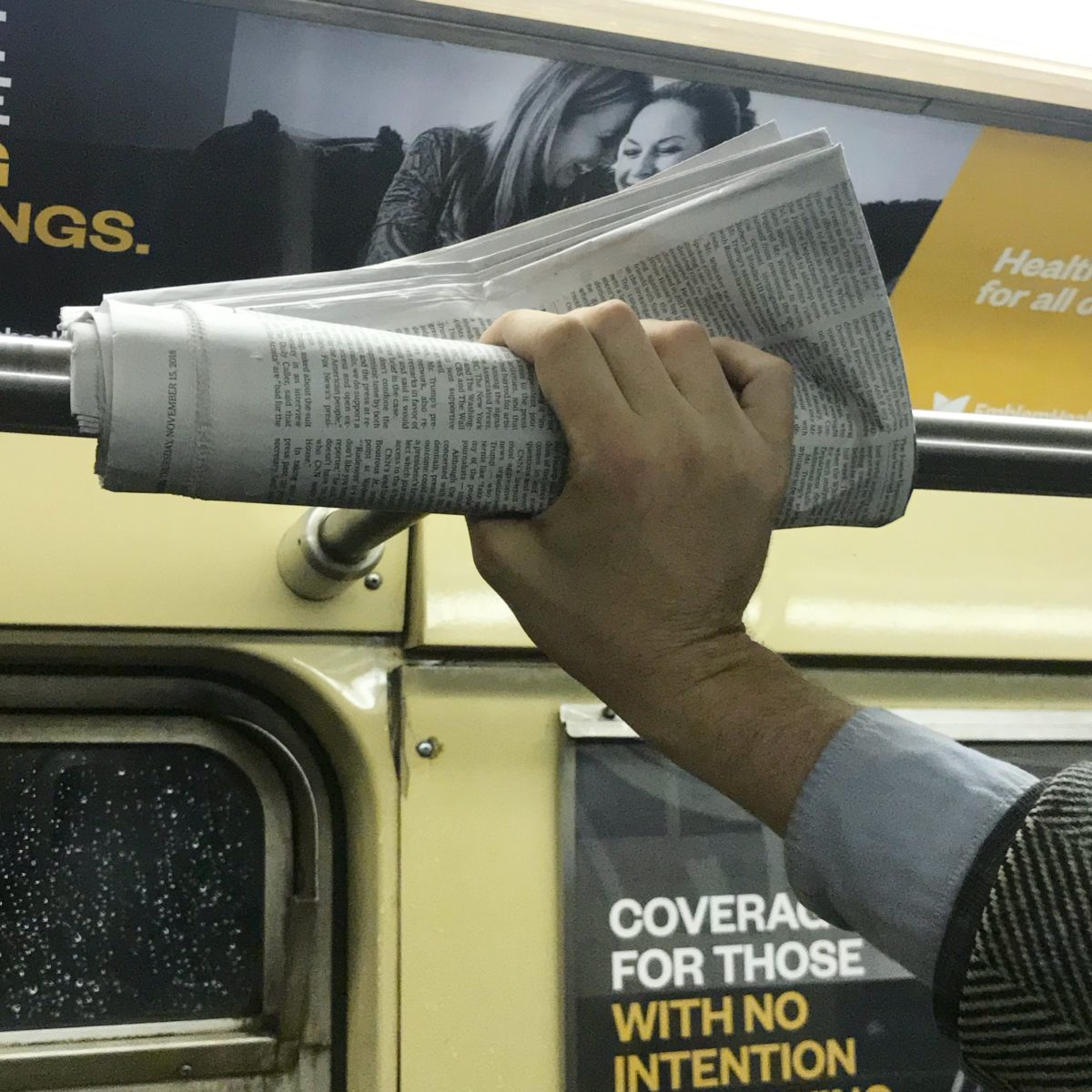 hand holding a newspaper against a subway rail