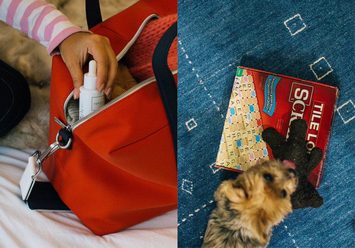 a woman packs a face serum into a red Everywhere Bag from Away's Chalet Collection. A dog sniffs a Scrabble board game box.