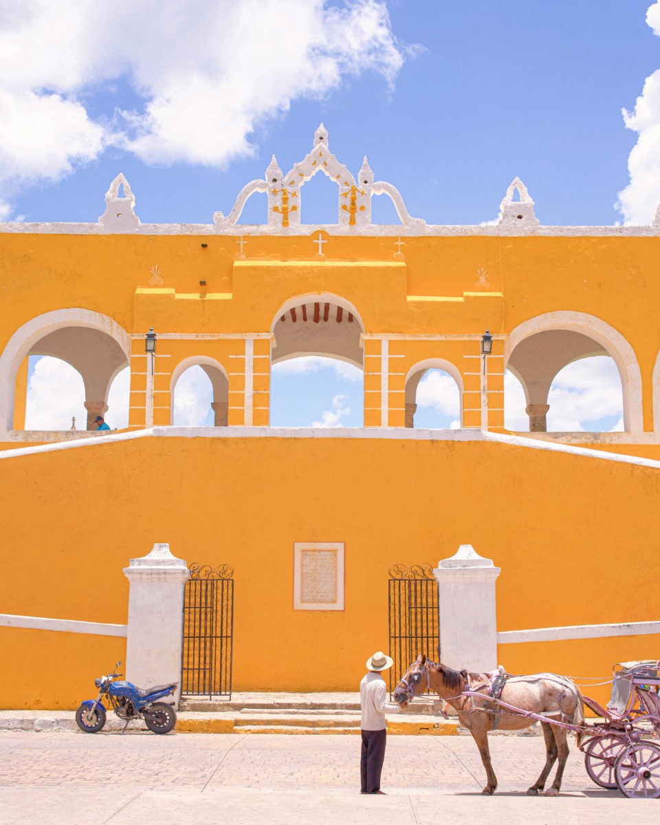 a person and a donkey walking past arches on a sunny day