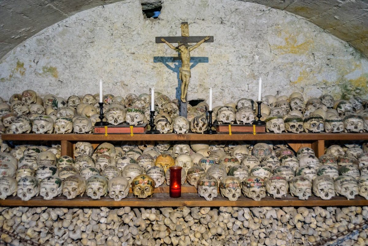 a cross sits above a long shelf of skulls and bones