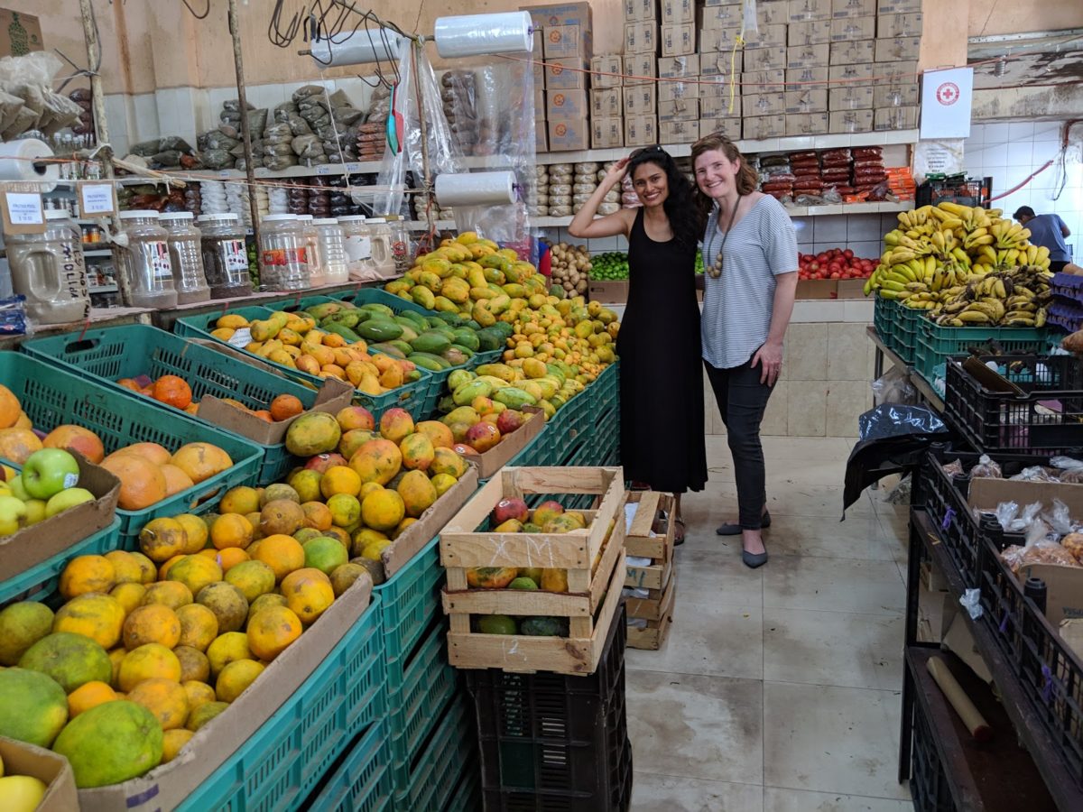 two women standing near a long fruit stand