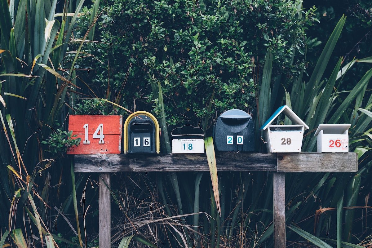 Five different looking mailboxes lined up next to each other with trees in the background