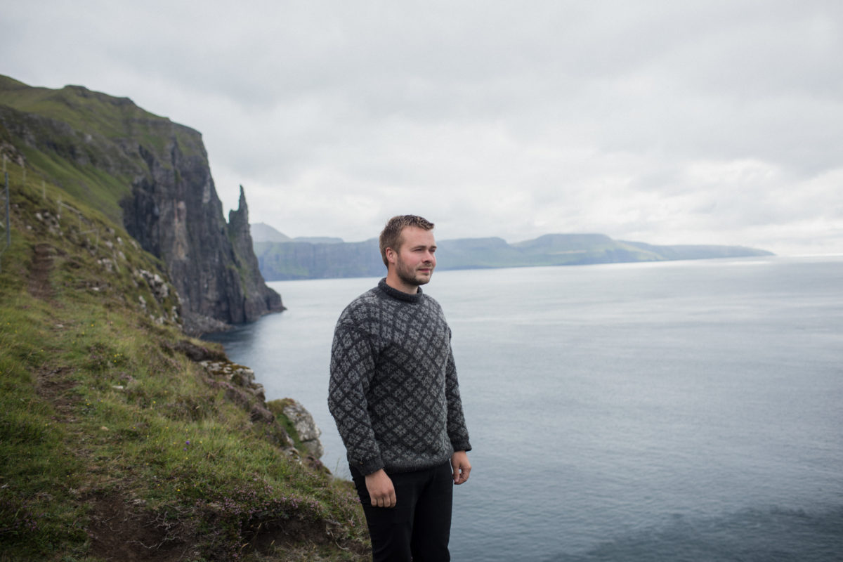 a man standing on a grassy cliff overlooking the ocean