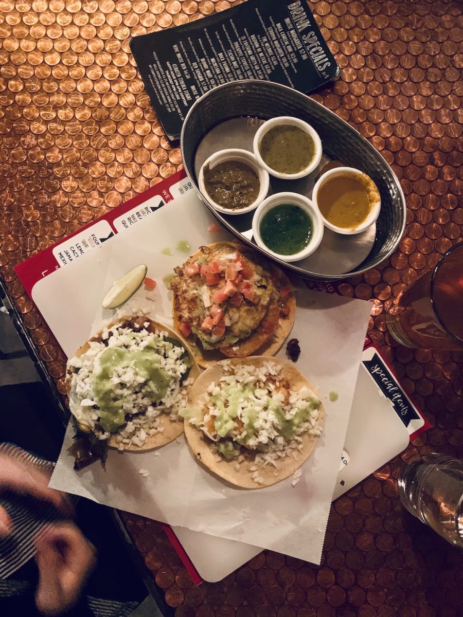 three various tacos and an assortment of four small salsas on a bar top