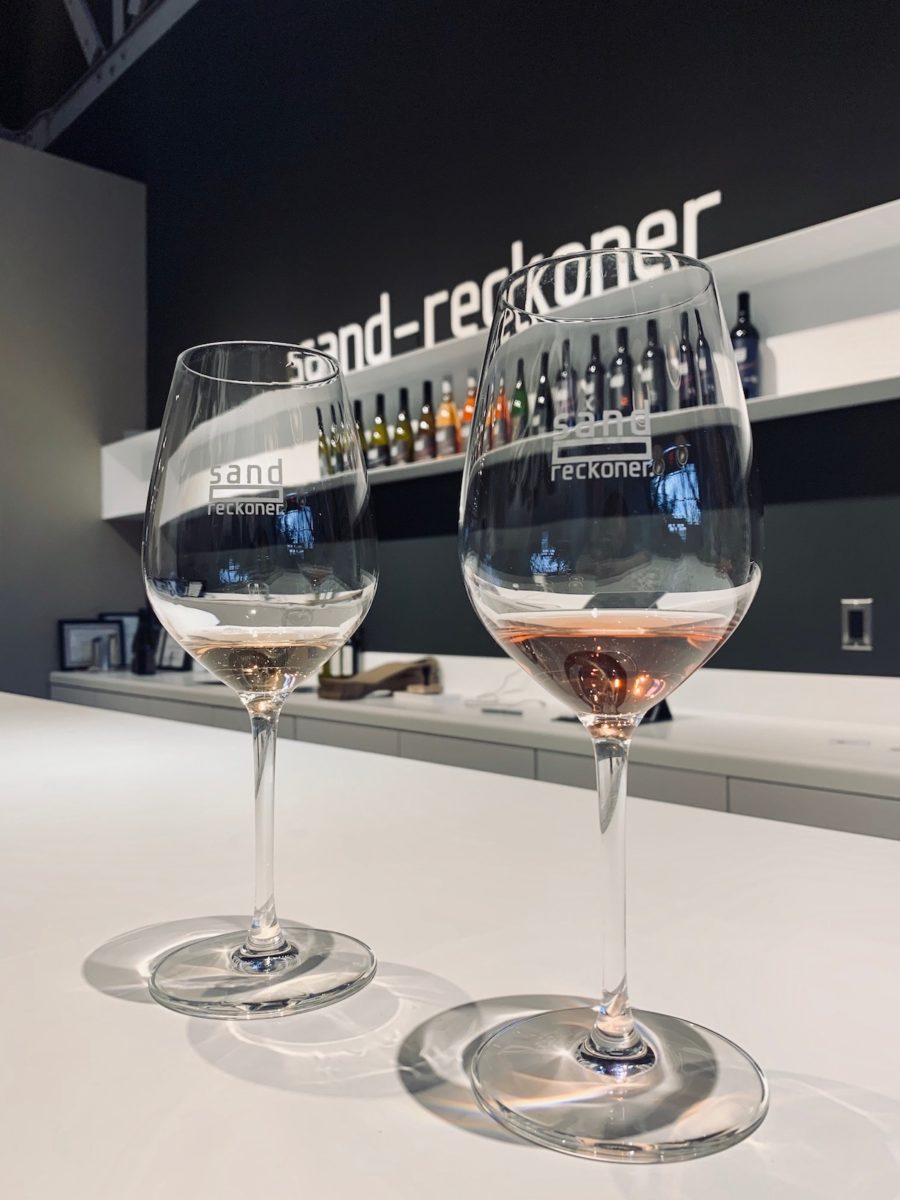 two glasses of wine, one with white and one with rosé, on a bar top with the Sand-Reckoner sign in the background